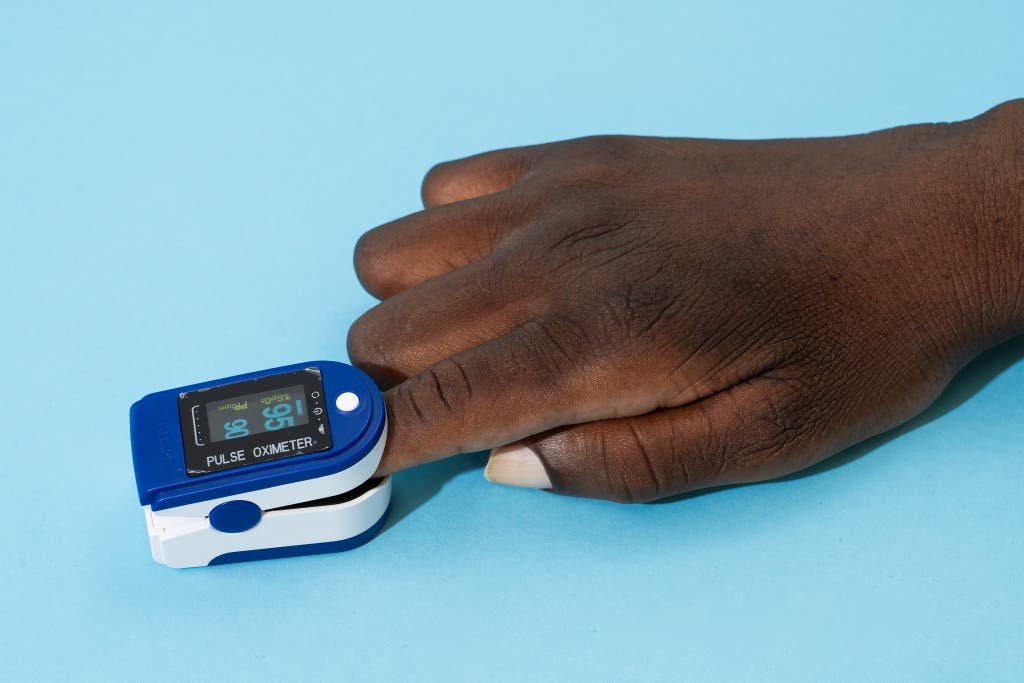 The iHealth Fingertip Pulse Oximeter on a person's finger with a light blue background